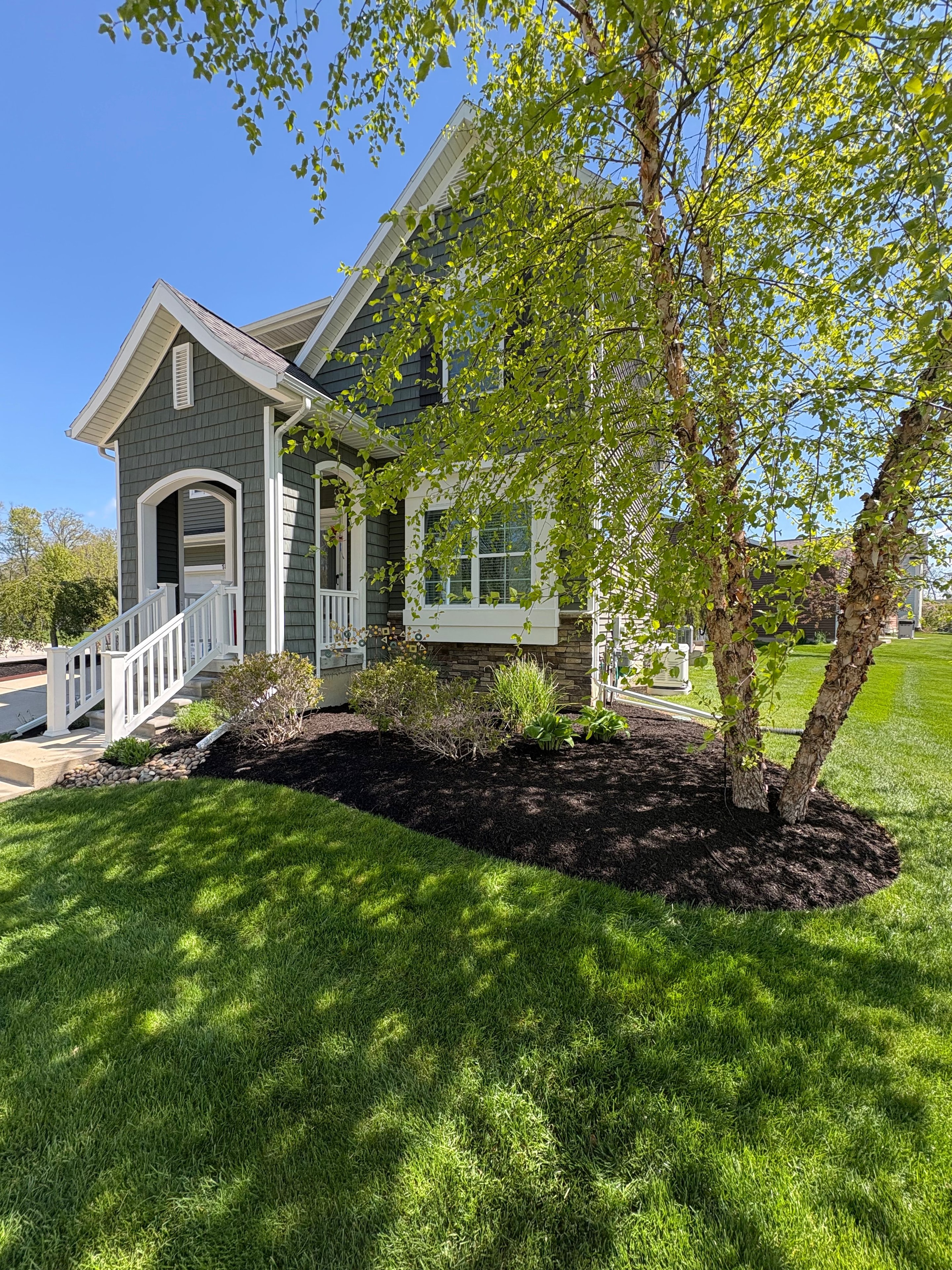 Fresh black mulch beds framing the front entry — clean edges, healthy plantings.